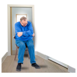 A person sitting alone on a chair in an empty room with the door shut behind him.