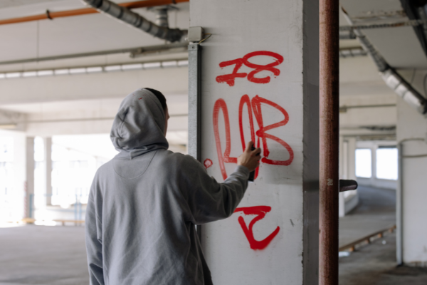 Hooded figure spray tagging a wall