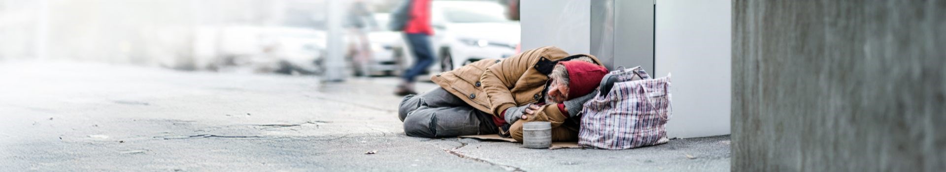 Man sleeping on pavement with bag of belongings